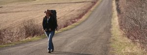 Dianne Whelan is walking toward the camera looking on the left her hands are on her belt and she's wearing a cowboy straw hat and backpack
