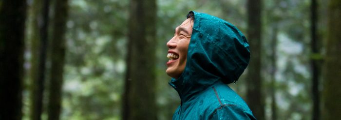 Man in teal rain jacket smiling in forest on a rainy day