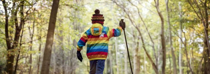 Young child in rainbow-coloured jacket hiking with trekking pole