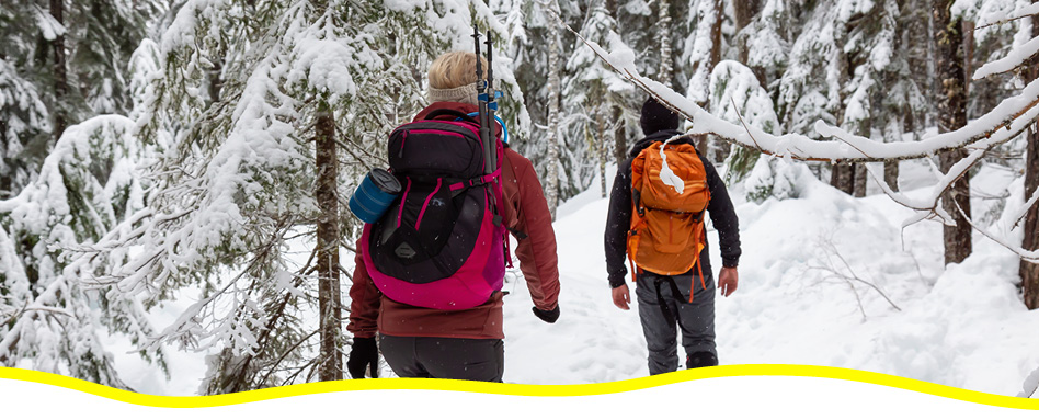 Two people with backpacks, hiking in the winter. Deux personnes avec des sacs à dos, en randonnée en hiver.
