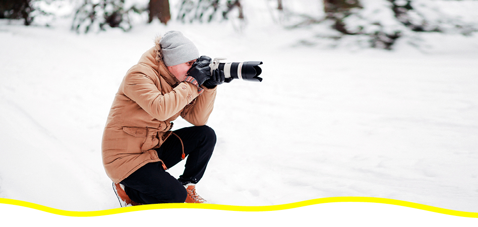Man kneeling down on a trail in the winter with a camera taking a picture
