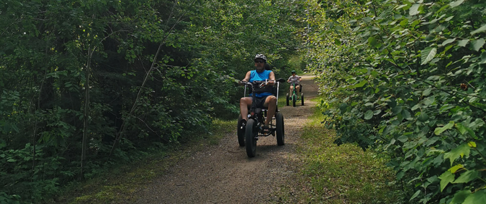 Adults on accessible bikes on a trail surrounded by trees