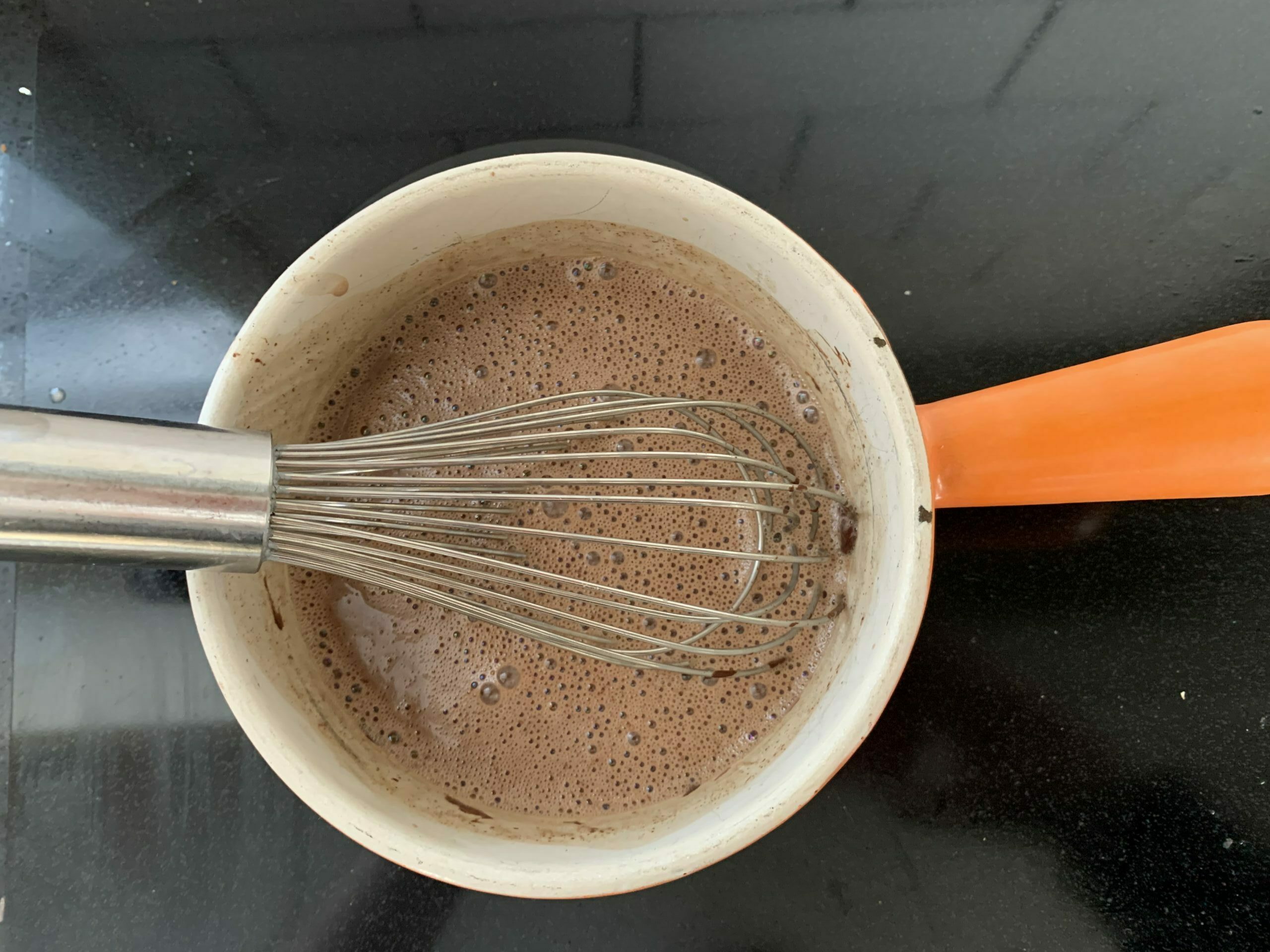 Image of a pot on the stove and a whisk stirring the hot chocolate inside
