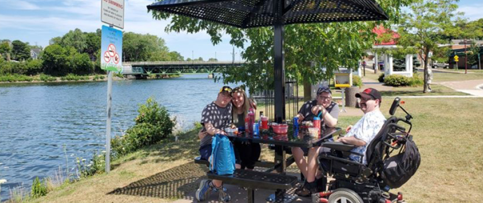 Four adults sitting at an accessible seating area off the trail and by the water in New Glascow, Nova Scotia 