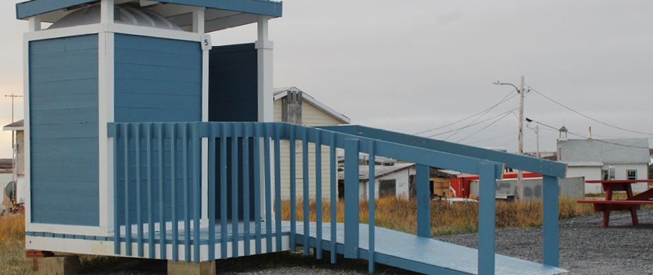A blue and white accessible outhouse that offers a wheelchair ramp for users. 
