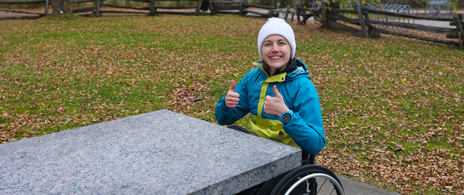 An adult in a wheelchair sitting at an accessible picnic table along a trail in Quebec City