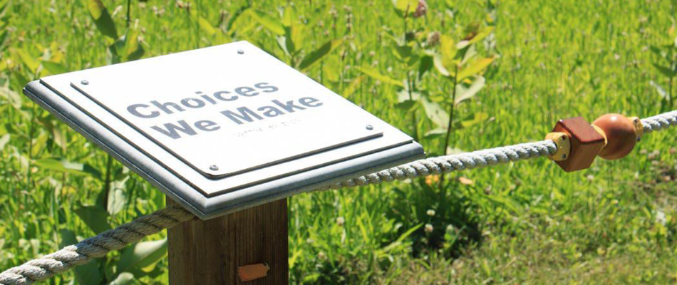 A sign along a trail the reads "Choices We Make." The sign is a part of a guided rope.