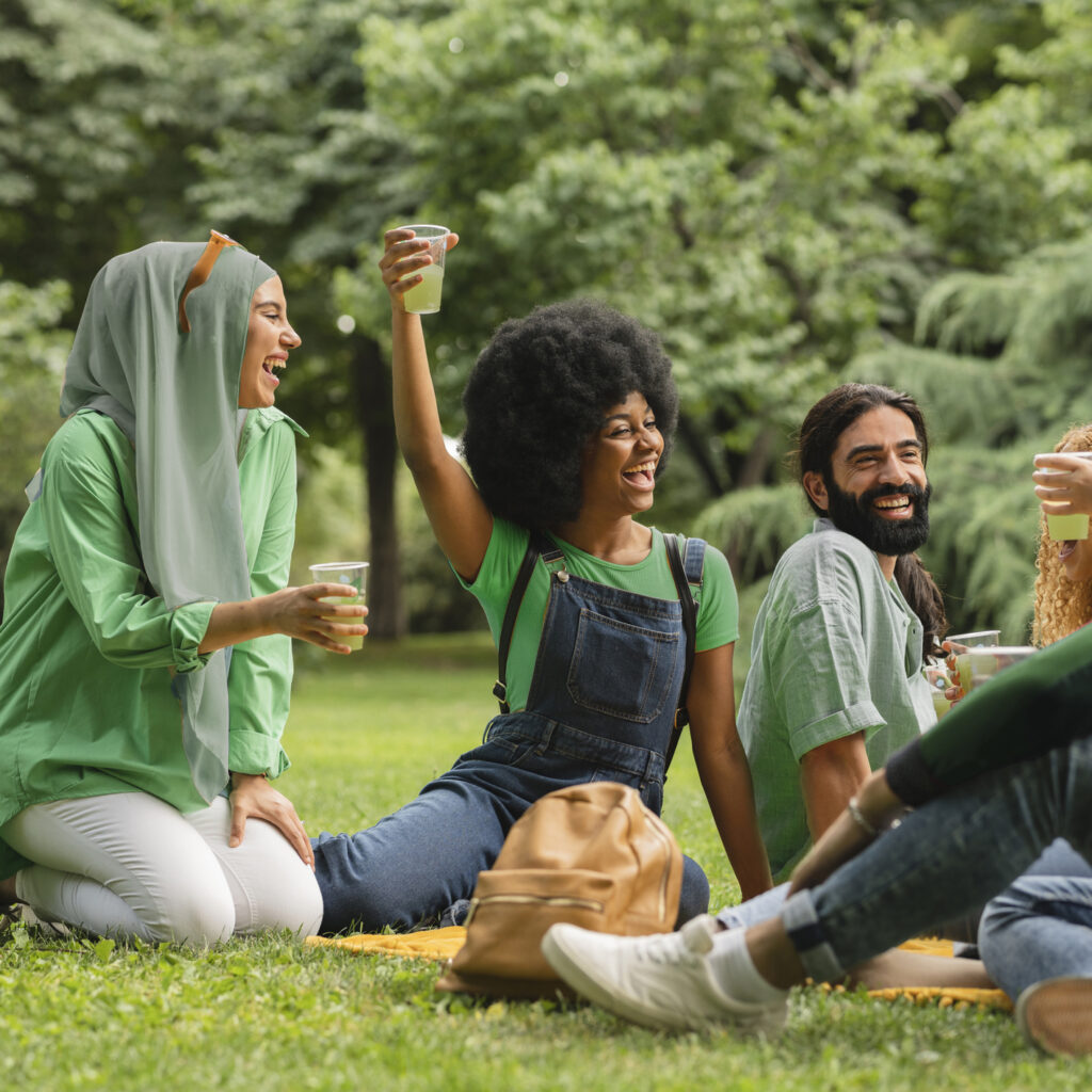A group of adults wearing green and holding clear cups with green liquid sitting on the grass participating in ways to go green for St. Patrick's day 
