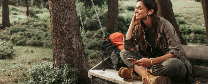 A female adult sitting on a bench with headphones in listening to music