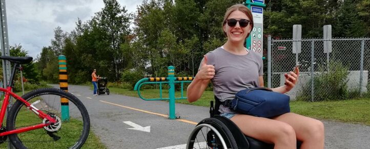 Woman using a wheelchair gives a thumbs up on an accessible trail