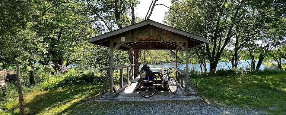 a bike leaning against a picnic table under a wooden gazebo 