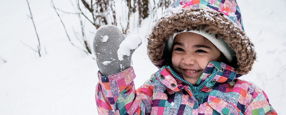 A child smiling holding snow in their glove. 