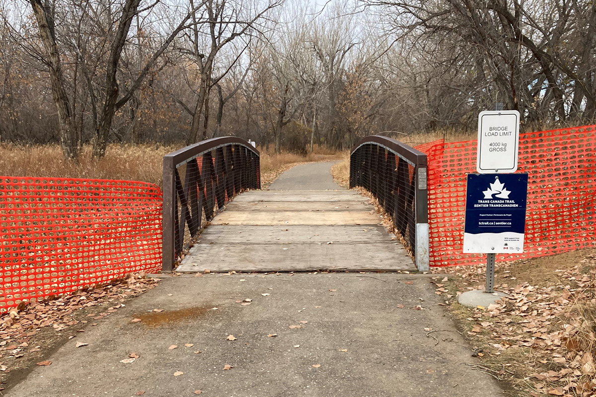 A tRans Canada Trail sign in front of a bridge with orange mesh fencing on both sides side.