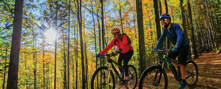 Two adults riding their bikes on a trail downhill on an autumn day