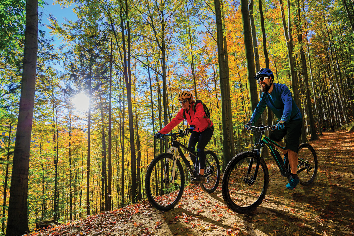 Two adults riding their bikes on a trail downhill on an autumn day