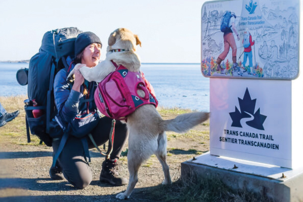 Melanie Vogel kneeling down to a dog in front of a Trans Canada Trail sign