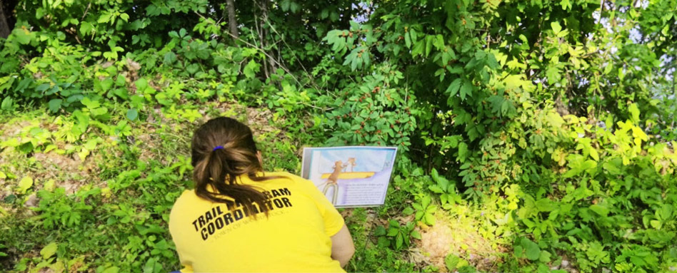 Trail Coordinator in front of a storybook poster on the trail