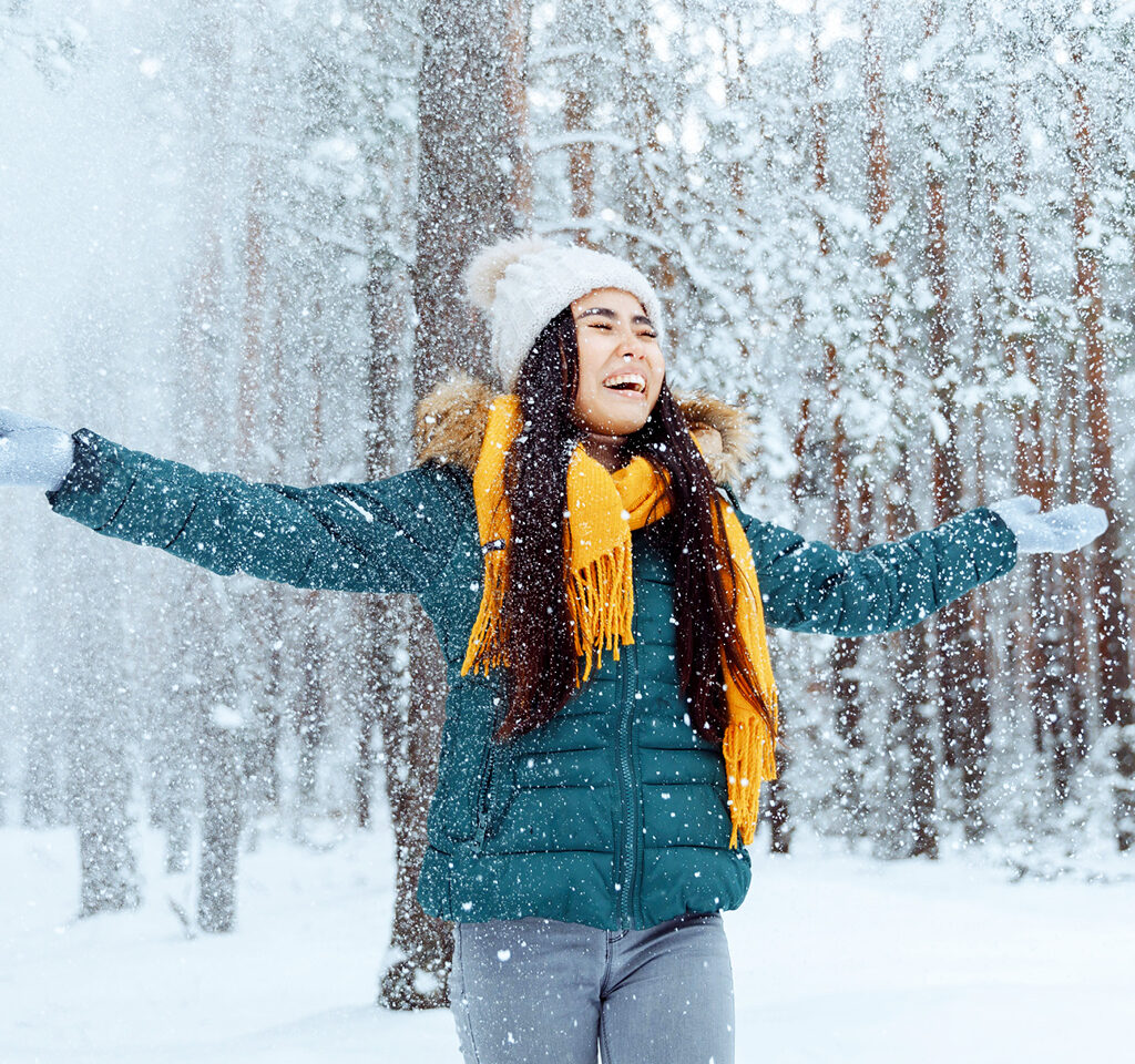 Joyful woman embracing the winter, arms outstretched on a scenic section of the Trans Canada Trail. Femme heureuse, bras écartés, sur un sentier en hiver.