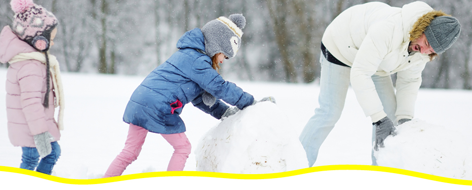 A family building a snowball for the base of a snowman. Une famille construisant une boule de neige pour la base d'un bonhomme de neige.
