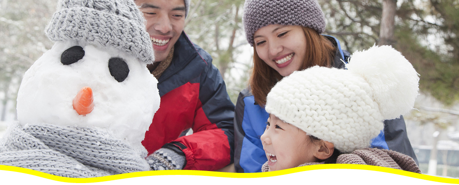 A family, with a laughing little girl, having fun building a snowman. Une famille, avec une petite fille qui rit, s'amuse à construire un bonhomme de neige.