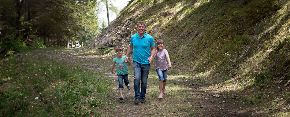  A man walking hand in hand with his two daughters along a green trailway.