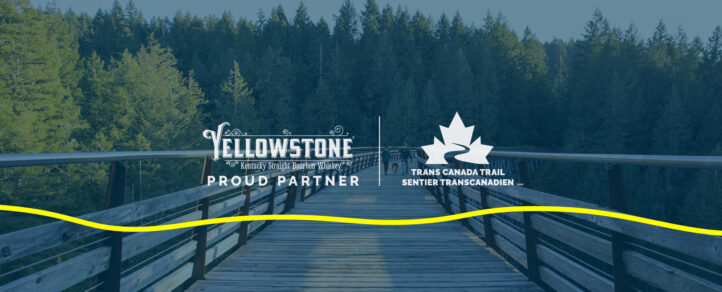 Yellowstone Bourbon and Trans Canada Trail Logos over an image of a wooded trail with a boardwalk running through it.
