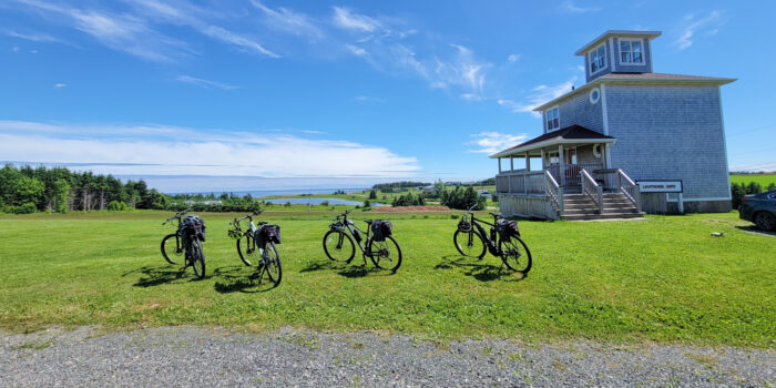 Bikes parked on a lush green lawn in Prince Edward Island overlooking the expansive water ahead | Vélos garés sur une pelouse verdoyante de l’Île-du-Prince-Édouard surplombant les vastes eaux devant nous.