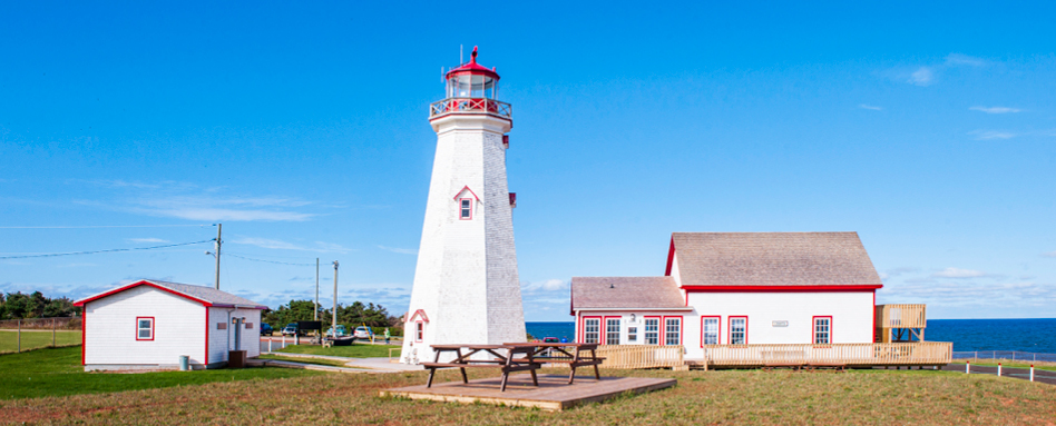 A white and red lighthouse standing tall at East Point. | Un phare blanc et rouge qui se dresse à East Point.