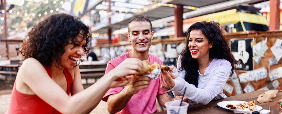 Three people enjoying tacos at an outdoor table. Trois personnes dégustant des tacos à une table en plein air.