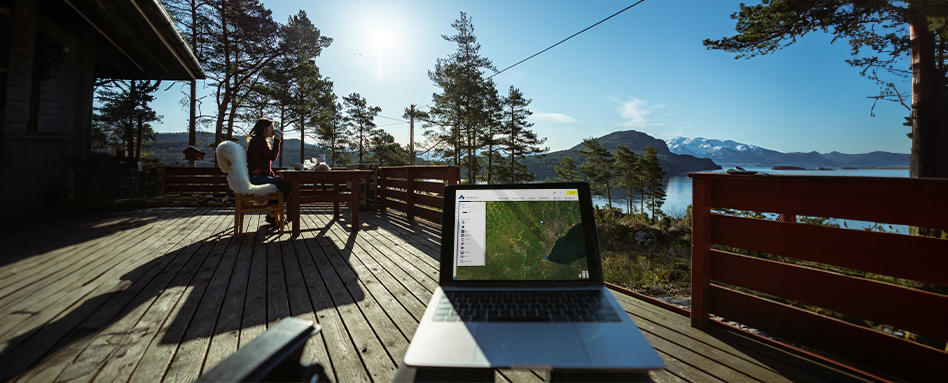 Laptop on wooden deck with mountain view, displaying Trans Canada Trail map. Ordinateur portable sur une terrasse en bois avec vue sur les montagnes, affichant la carte du sentier Transcanadien.