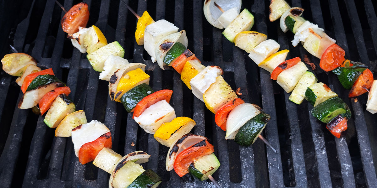 A grill featuring an array of colorful vegetable skewers, sizzling and ready for cooking outdoors. Un gril avec un assortiment de brochettes de légumes colorées, grésillantes et prêtes à être cuites en plein air.