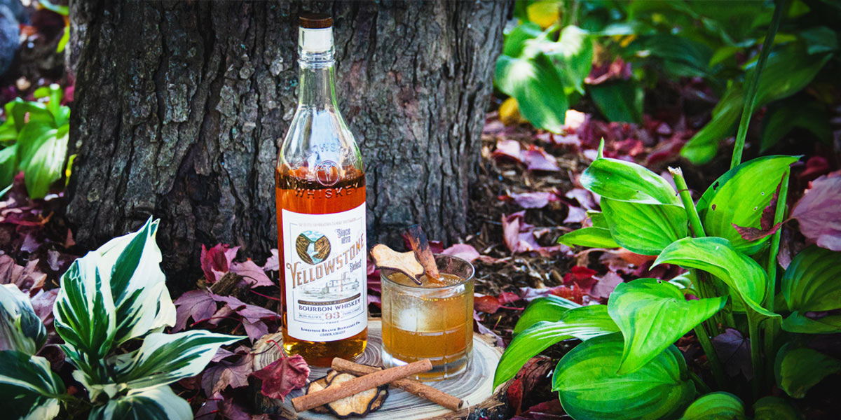 A bottle of Yellowstone Bourbon and a glass of juice placed on the ground, showcasing a blend of spirits and refreshment. Une bouteille de Yellowstone Bourbon et un verre de jus posés au sol, mettant en valeur un mélange de spiritueux et de rafraîchissements.