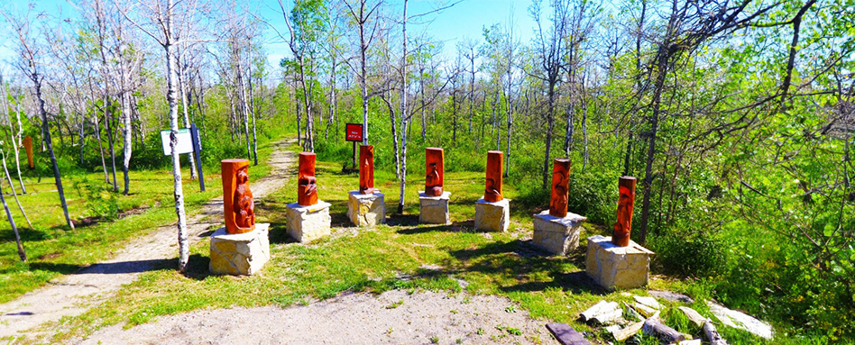 Red totem poles are positioned amidst the dense foliage of the forest along the Bebamikawe Memorial Trail. Des totems rouges sont positionnés au milieu du feuillage dense de la forêt le long du Bebamikawe Memorial Trail.