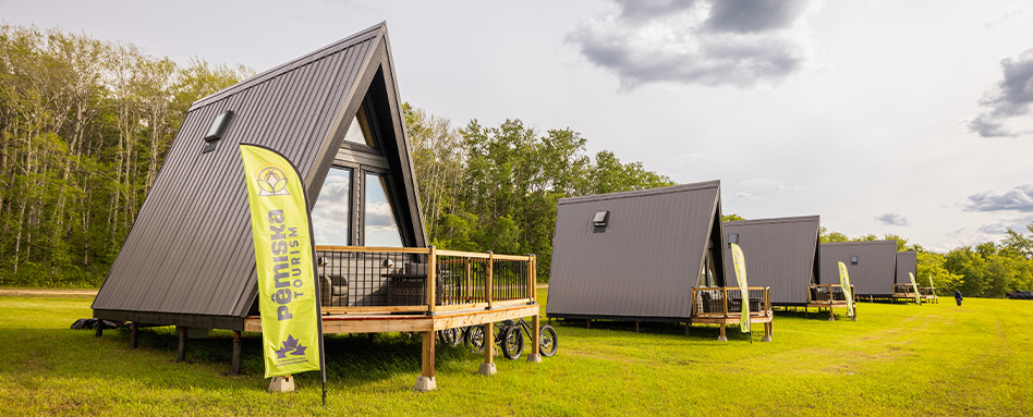 A picturesque view of three tiny lodges on the grass at Pemiska Trail. Une vue pittoresque de trois petits pavillons sur l'herbe à Pemiska Trail. 