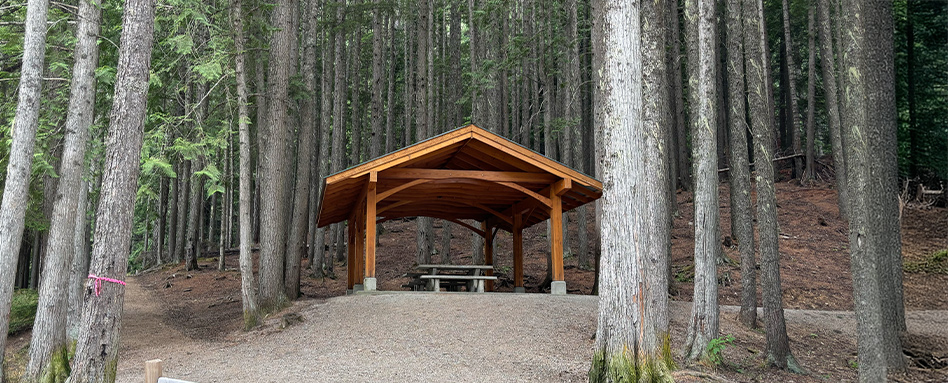 A picnic shelter nestled among trees in the woods, located along the Great Northern Rail Trail. Un abri de pique-nique niché parmi les arbres dans les bois, situé le long du Great Northern Rail Trail.