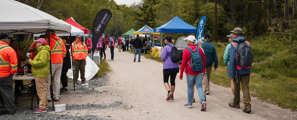 Attendees stand near tents at the outdoor event on Rum Runners Trail. Les participants se tiennent près des tentes lors de l'événement en plein air sur Rum Runners Trail. 