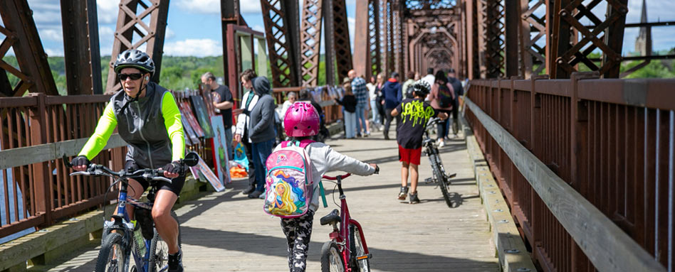 Cyclists ride across the Bill Thorpe Walking Bridge, showcasing camaraderie and the beauty of the outdoors. Des cyclistes traversent le pont piétonnier Bill Thorpe, mettant en valeur la camaraderie et la beauté du plein air.