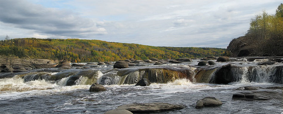 A serene view of the Athabasca River, featuring rocks and cascading waterfalls amidst a lush forest backdrop. Une vue sereine de la rivière Athabasca, avec des rochers et des cascades en cascade au milieu d'un décor de forêt luxuriante.