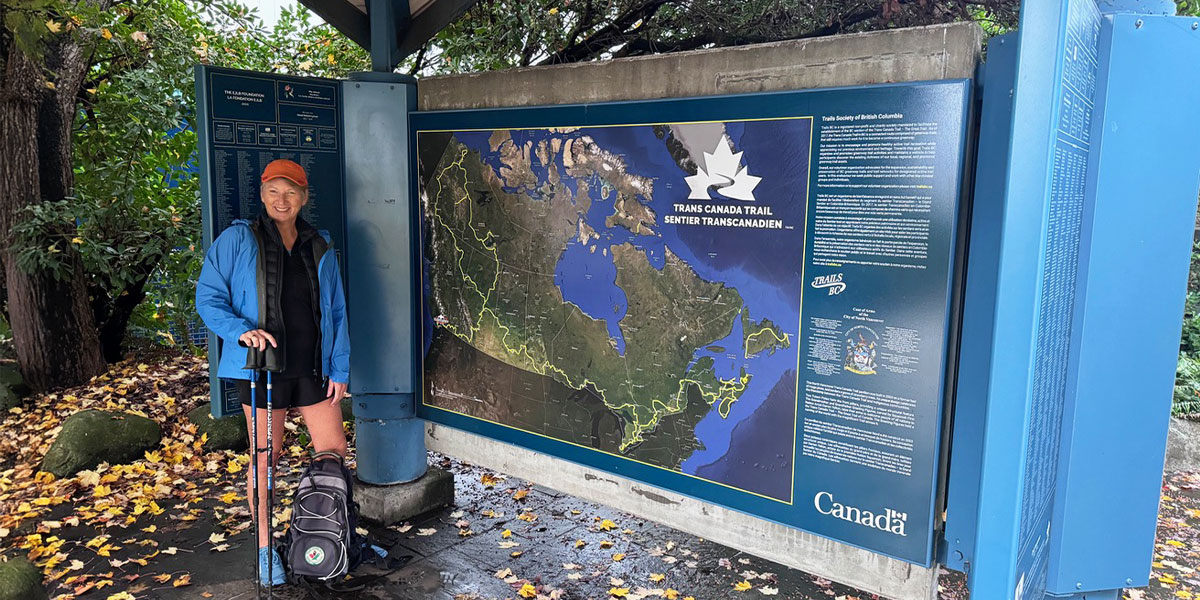 Mary Charleson stands beside a Trans Canada Trail map, highlighting the scenic routes across Canada. Mary Charleson se tient à côté d'une carte du Sentier Transcanadien, mettant en valeur les itinéraires pittoresques à travers le Canada.