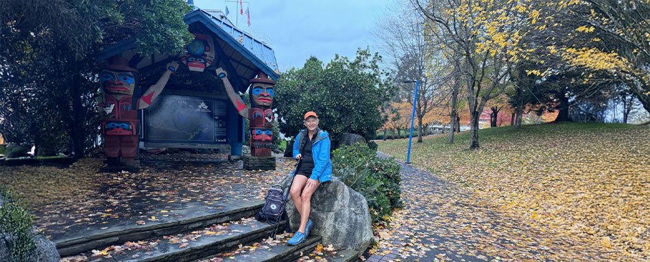 Mary Charleson sits on steps beside a totem pole, showcasing cultural heritage and serene surroundings. Mary Charleson est assise sur des marches à côté d'un totem, illustrant le patrimoine culturel et un cadre paisible.