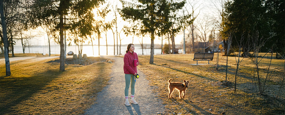 A woman and her dog enjoy a leisurely walk in a park at sunset. Une femme et son chien profitent d’une promenade paisible dans un parc au coucher du soleil.