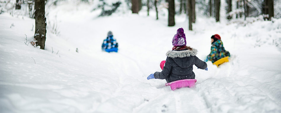 Three children gleefully sled down a snowy trail, enjoying a fun winter day. Trois enfants dévalent joyeusement un sentier enneigé en luge, savourant une journée d’hiver ludique.