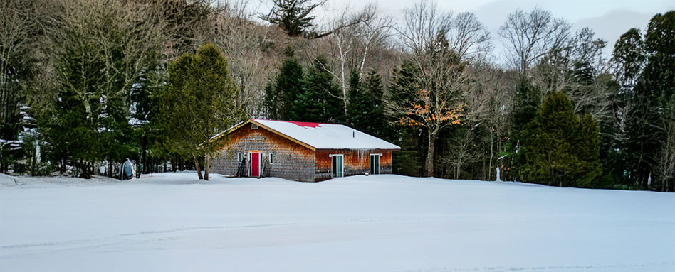 A small warming hut stands alone in a vast snowy field. Un petit abri chauffé se dresse seul dans une vaste étendue enneigée.