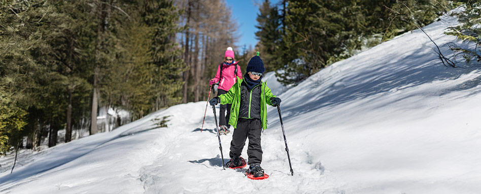 Two individuals on snowshoes navigate a snow-covered hill, showcasing their skills in a winter landscape. Deux personnes en raquettes descendent une colline enneigée, démontrant leur habileté dans un paysage hivernal.