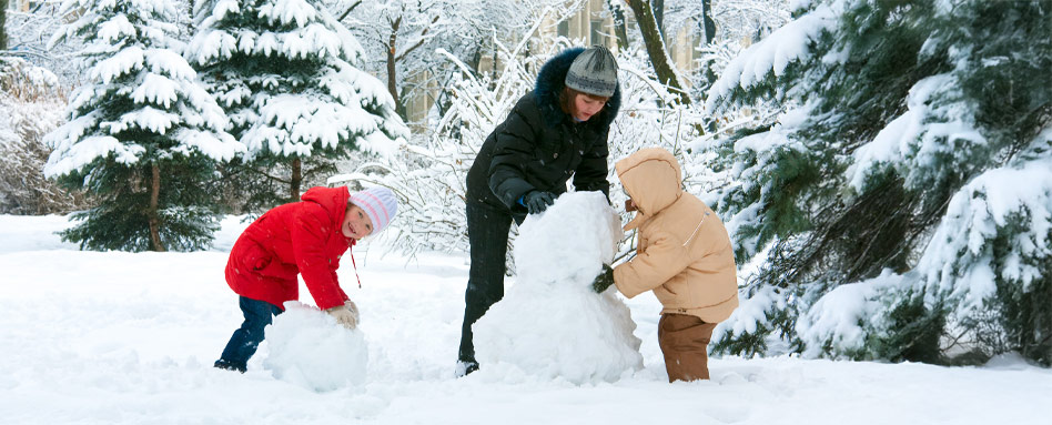 A women and two kids joyfully constructing a snowman together on a family day in a snowy landscape. Une femme et deux enfants construisent joyeusement un bonhomme de neige ensemble lors d’une journée en famille dans un décor enneigé.