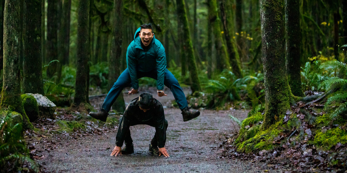 men playfully jumping overtop of one another in a rainy forest