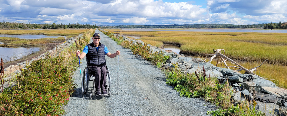 man in a wheelchair smiling on a path beside a marsh
