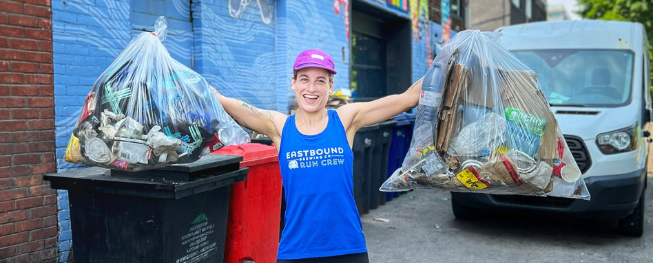 person smiling in running gear holding up trash bags