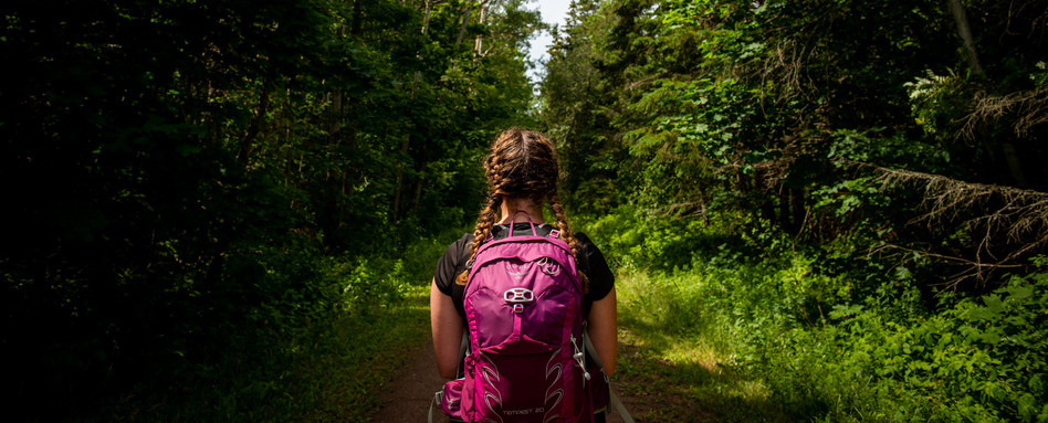 woman wearing backpack staring into a forest
