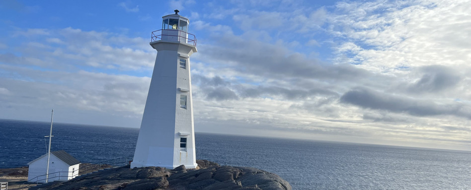 white lighthouse at Cape Spear, Newfoundland and Labrador—the easternmost point in Canada—overlooking the Atlantic Ocean under a partly cloudy sky. | Phare blanc au cap Spear, à Terre-Neuve-et-Labrador – le point le plus à l’est du Canada – surplombant l’océan Atlantique sous un ciel partiellement nuageux.